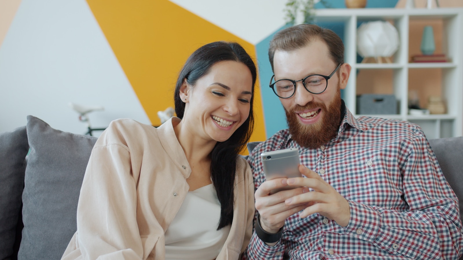 Couple laughing while looking at a smartphone together.