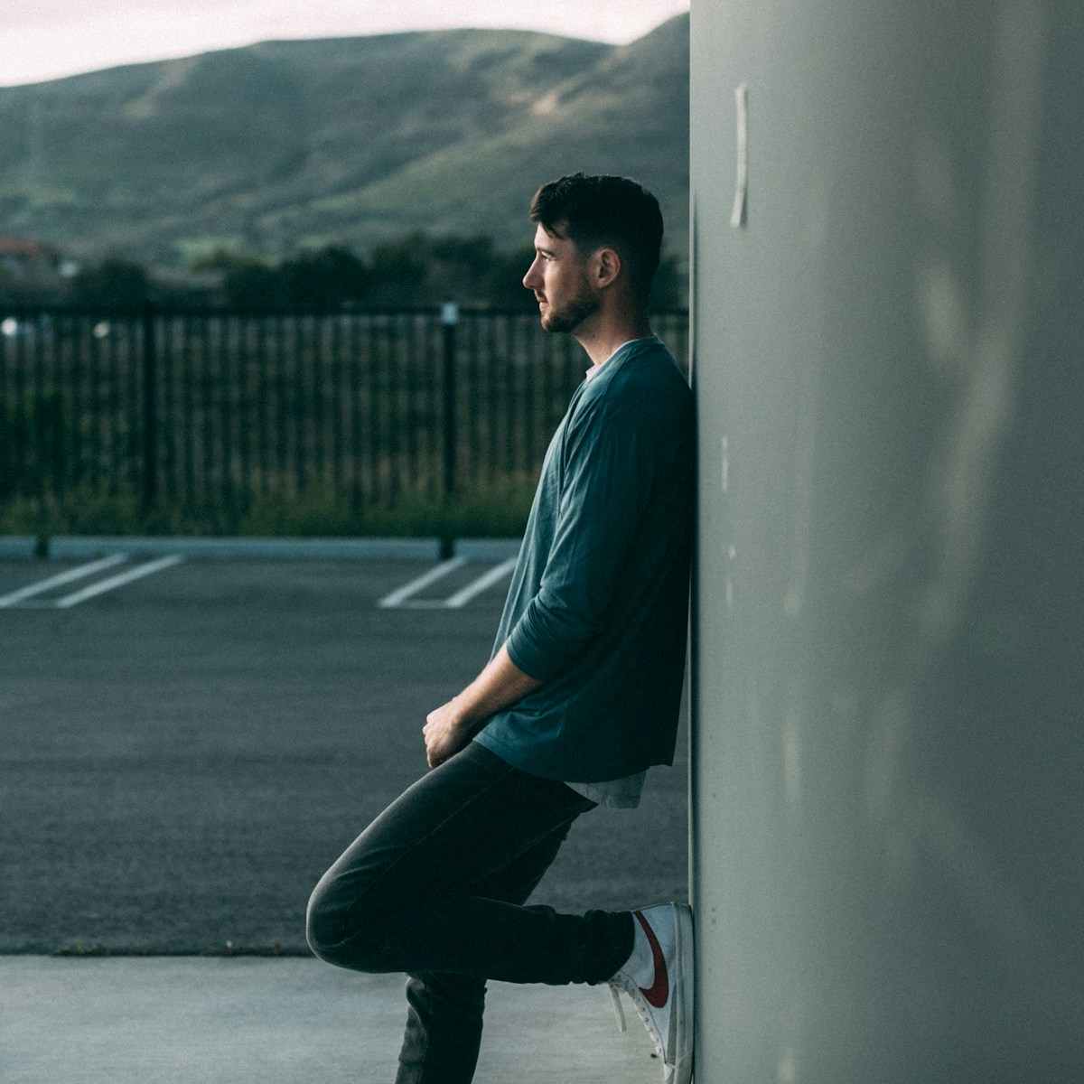 a man leaning against a wall in a parking lot