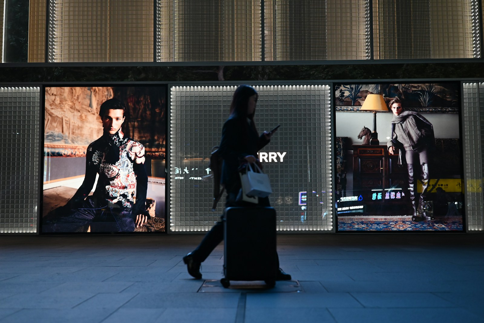 Person walks past illuminated fashion displays at night.