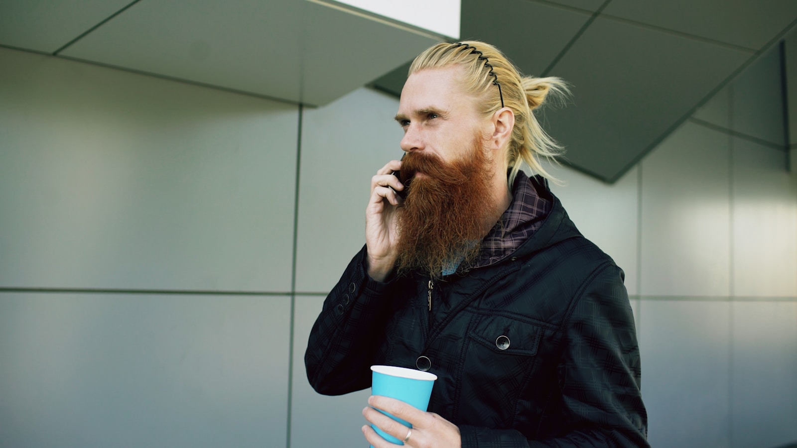 Man with beard talking on phone holding coffee cup