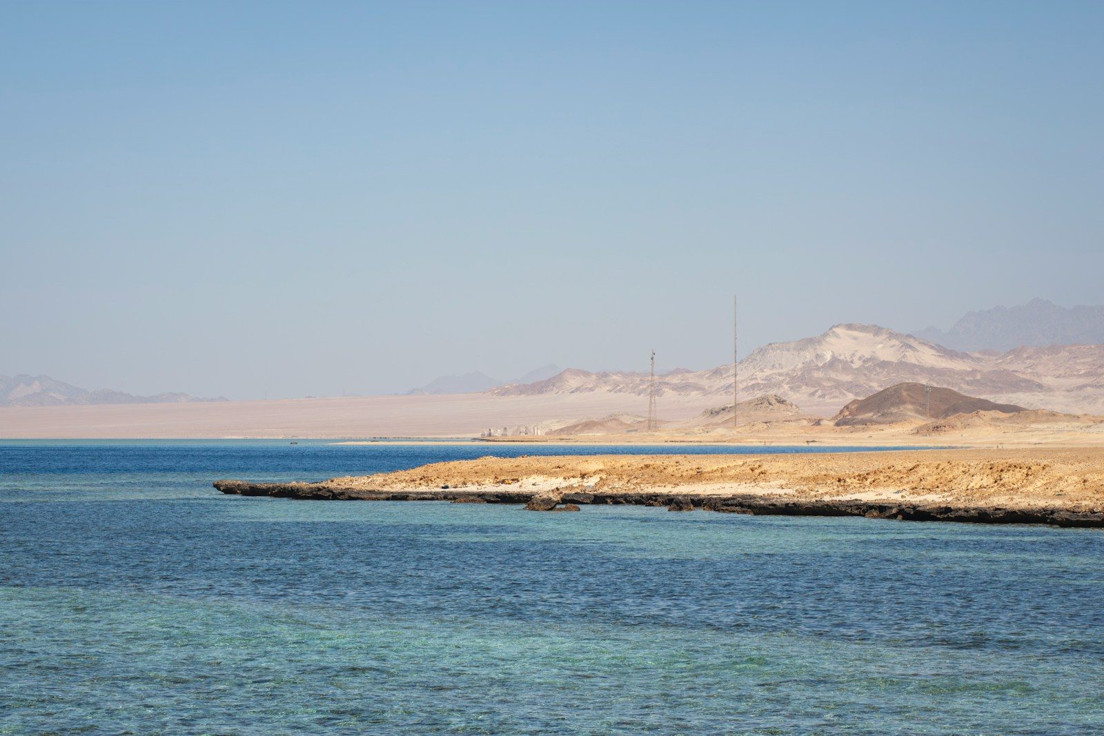 Clear blue water meets a sandy coastline with distant mountains